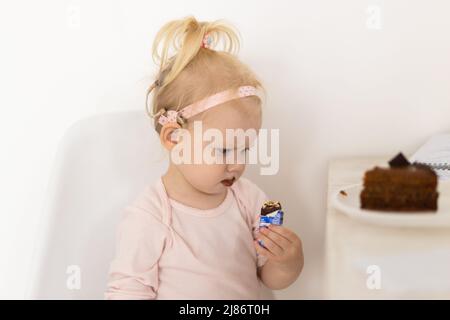 Bambino divertente con impianto cocleare seduta a casa e mangiare. Ascolta il concetto di tecnologia innovativa di aiuto e medicina Foto Stock