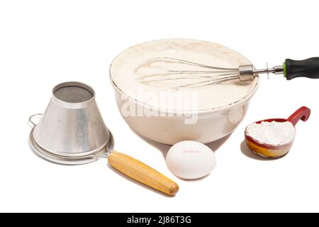 Mescolare gli ingredienti da forno in un recipiente, con uova, lievito secco e setaccio per setacciare la farina isolata su sfondo bianco. Foto Stock