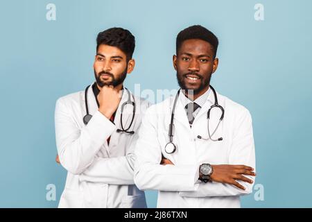 ritratto di medico sorridente in camice bianco da laboratorio con stetoscopio che conferisce con il giovane medico su sfondo blu Foto Stock