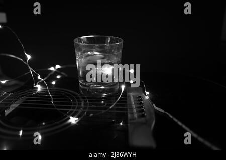 su una chitarra c'è un bicchiere di whiskey con cubetti di ghiaccio in bianco nero Foto Stock