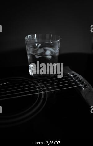 su una chitarra c'è un bicchiere di whiskey con cubetti di ghiaccio in bianco nero Foto Stock