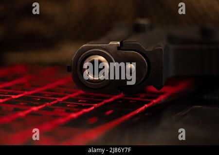 La pistola si trova su una tastiera nera per laptop con retroilluminazione rossa, minaccia alla sicurezza, cyber attacco, hacking del sistema Foto Stock