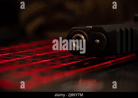 La pistola si trova su una tastiera nera per laptop con retroilluminazione rossa, minaccia alla sicurezza, cyber attacco, hacking del sistema Foto Stock