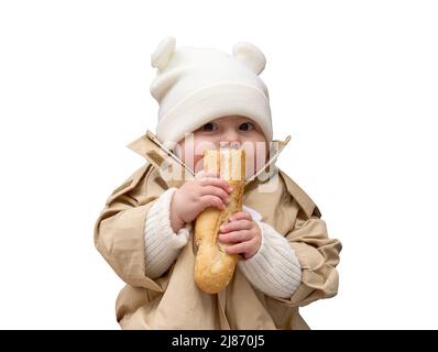 Ragazza cute del bambino vestita in berretto, maglione e cappotto che mangia baguette. Isolato su sfondo bianco. Foto Stock