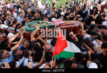 Gerusalemme, Medio Oriente. 13th maggio 2022. I palestinesi ondano bandiere nazionali mentre trasportano la scrigno del giornalista ucciso al-Jazeera Shireen Abu Aklel durante la sua processione funebre dalla chiesa verso il cimitero, a Gerusalemme, Israele, venerdì 13 maggio 2022. Abu Akleh è stato ucciso il 11th maggio, mentre copriva un raid nella Cisgiordania occupata da Israele. Foto di Jamal Awad/UPI Credit: UPI/Alamy Live News Foto Stock