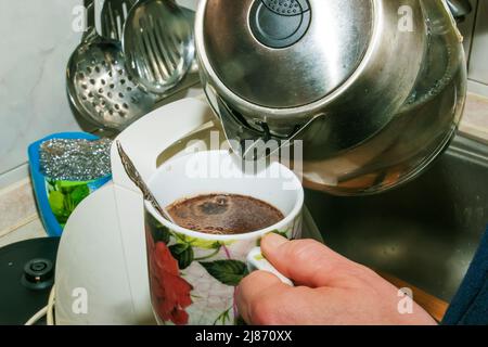 Una donna versa l'acqua calda da un bollitore elettrico in una tazza di caffè. Foto Stock