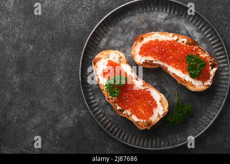 Due dandwiches con caviale rosso. Caviale rosso salmone in ciotola e sandwich server su vecchio piatto di ferro su sfondo vecchio tavolo nero. Vista dall'alto. Spazio di copia. Foto Stock