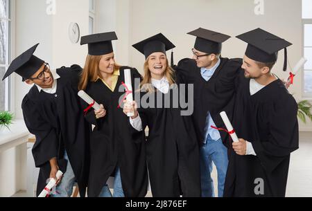 Un gruppo di amici universitari felici che si abbraccia e si diverte alla loro laurea Foto Stock