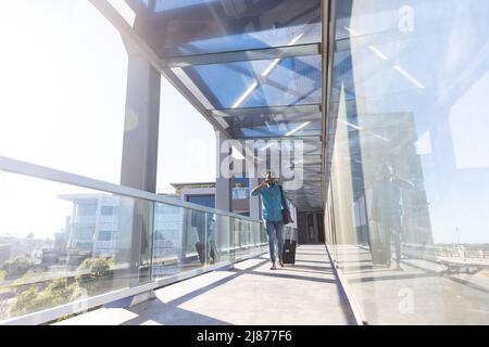 Tutta la lunghezza del giovane uomo d'affari afroamericano che cammina con i bagagli nel corridoio all'aeroporto Foto Stock