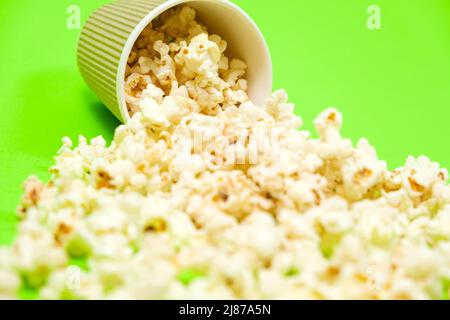 Il popcorn fuoriesce da una tazza di carta marrone su uno sfondo verde da vicino Foto Stock