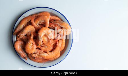 Piatto bianco pieno di gamberi cotti su sfondo bianco. Spazio di copia. Vista dall'alto. Foto Stock