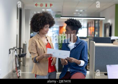 Le donne d'affari multirazziali si guardano mentre discutono sopra documento sul posto di lavoro Foto Stock