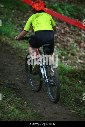 Giovane ciclista su una Mountain bike nel fango pedala con sforzo in salita durante la gara ciclista Foto Stock