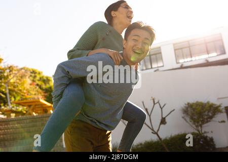 Giocoso giovane uomo asiatico piggybacking ragazza in cantiere durante la giornata di sole, spazio copia Foto Stock