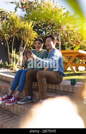 Allegro giovane coppia asiatica che si gode il tempo libero mentre si guarda il tablet digitale nel cortile Foto Stock