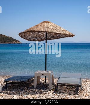 Ombrellone in vimini e due lettini vuoti sulla spiaggia. Concetto di vacanza. Orizzontale. Foto Stock