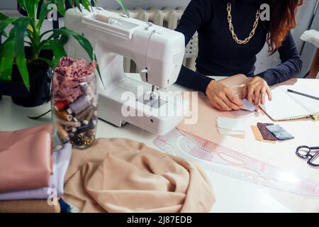 in un notebook scrivono splendidi marinai con capelli lunghi. il sarto crea una collezione di abiti. abbigliamento giovane donna designer con cui lavorare Foto Stock