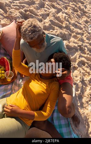 Alto angolo di vista di felice afroamericana matura donna sdraiata sul braccio di uomo anziano su spiaggia sabbiosa Foto Stock