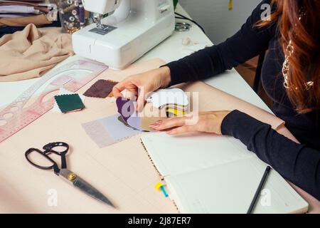 in un notebook scrivono splendidi marinai con capelli lunghi. il sarto crea una collezione di abiti. abbigliamento giovane donna designer con cui lavorare Foto Stock