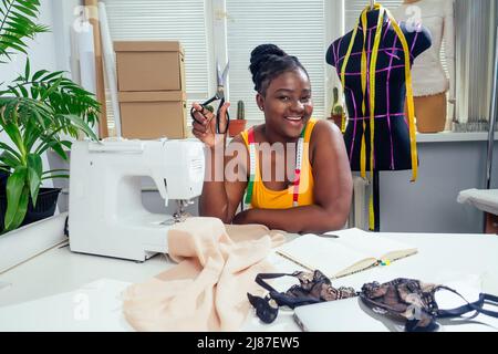 Giovane donna dressmaker afroamericano cucire i vestiti su macchina da cucire a sarto ufficio esso tropicale estate stile Foto Stock