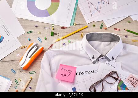 Scrivania con camicia con cucitrice e occhiali vista dall'alto. Graffette con penna e diagramma. Foto Stock