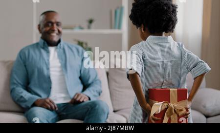 Little african american amorevole figlia nasconde scatola dà dono al papà amato il compleanno o il giorno del padre si congratula con il genitore sorpreso felice papà Foto Stock