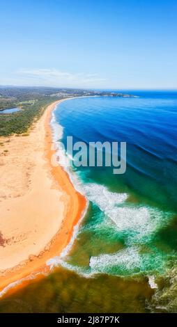 Lungo tratto curvo di spiaggia sabbiosa di Tathra sulla costa Sapphire del pacifico Australiano - panorama marino verticale aereo. Foto Stock