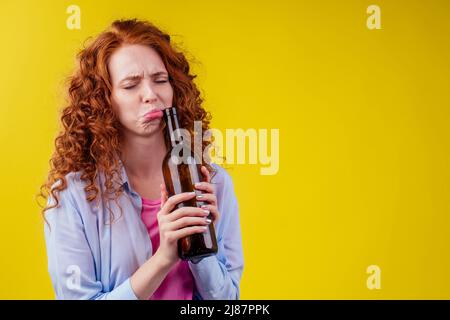 donna zenzero ricurly redhead bere birra e sentire cattivo umore in csudio giallo sfondo Foto Stock