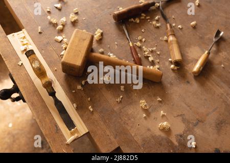 Vista ad angolo elevato del mazzuolo e di vari utensili manuali con trucioli di legno in officina Foto Stock