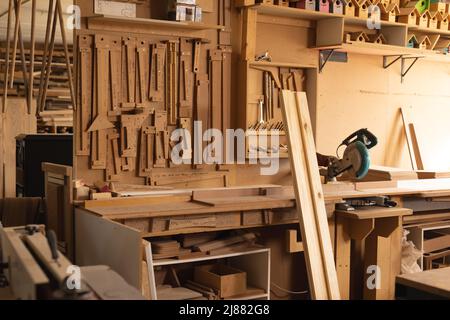 Interno dell'officina con assi e vari attrezzi per la lavorazione del legno appesi su scaffale in officina Foto Stock