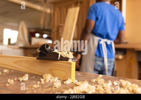 Primo piano di piallatrice su legno con falegname maturo afroamericano sullo sfondo Foto Stock