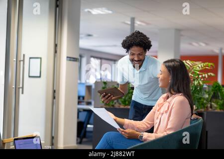 Sorridenti professionisti multirazziali che parlano di documenti al posto di lavoro moderno Foto Stock