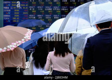 Tokyo, Giappone. 13th maggio 2022. La gente che tiene gli ombrelli cammina davanti ad uno schermo che mostra gli indici azionari medi e mondiali di Nikkei fuori di un brokerage, in mezzo alla pandemia di coronavirus a Tokyo. Credit: SOPA Images Limited/Alamy Live News Foto Stock