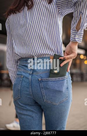 Donna sicura che si posa in salvo mantenendo il portafoglio nella tasca posteriore in pantaloni Foto Stock