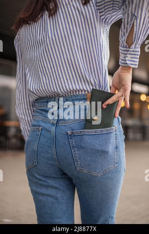 Donna sicura che si posa in salvo mantenendo il portafoglio nella tasca posteriore in pantaloni Foto Stock