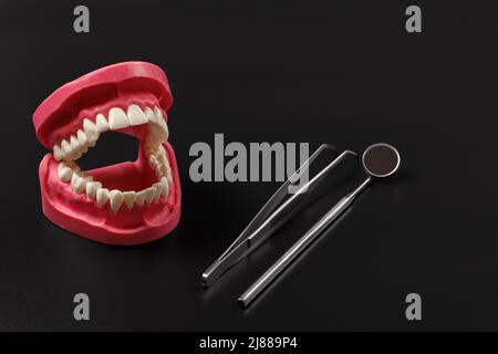 Set di strumenti metallici per il trattamento dentale con disposizione della mandibola umana. Pinzette e uno specchio sulla bocca su sfondo nero. Strumenti medici. Foto Stock