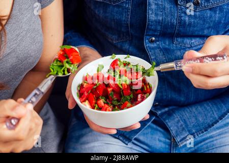 Giovane coppia indiana seduta in soggiorno e mangiare insalata di verdure Foto Stock