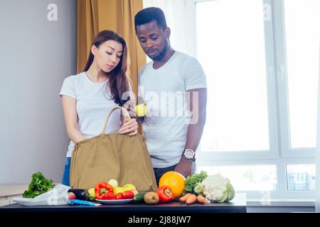 coppia multinazionale che scarica una borsa da prodotti che scelgono tessuto o poliestere bag.african american uomo e donna asiatica che viene a casa dopo il negozio Foto Stock