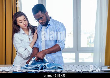 uomo africano americano e donna asiatica vestiti stirare insieme nel soggiorno Foto Stock