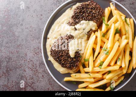 Bistecca arrosto Au Poivre e ricca salsa di Cognac servita con patatine fritte da vicino in un piatto sul tavolo. Vista dall'alto orizzontale Foto Stock