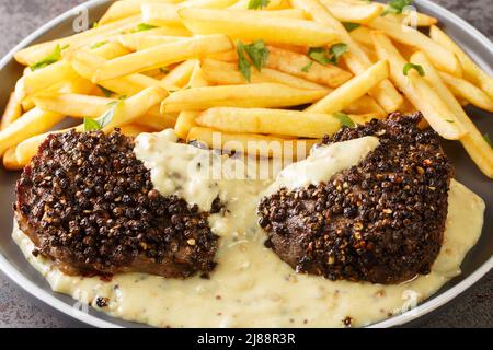 Il classico piatto francese bistecca au poivre è un mignon di filetto con una crosta croccante di mais e una ricca salsa di Cognac servita con patatine fritte da vicino in un pla Foto Stock