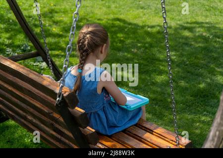 Adorabile bambina seduta su un altalena e pittura, vista posteriore Foto Stock