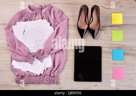 Blusa rosa con vista dall'alto, piatta e posata, con carte da lavoro e scarpe. Tablet con note adesive sulla scrivania. Foto Stock