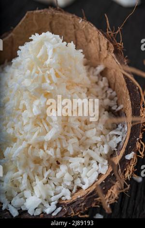 Cocco tritato su sfondo di legno, vista dall'alto. Latte di cocco e fiocchi di cocco sono cibi tropicali Foto Stock