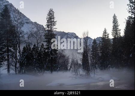 La valle di Yosemite è circondata da un sottile strato di nebbia che si estende sul fiume merced, fornendo un'atmosfera inquietante intorno al tramonto. Foto Stock