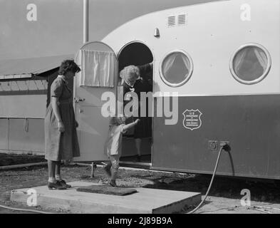 La giovane madre porta il suo bambino nella clinica del rimorchio il giorno in cui il medico sarà nel campo per esaminare alcuni dei bambini. Merrill, contea di Klamath, Oregon. Campo FSA (Farm Security Administration). Foto Stock