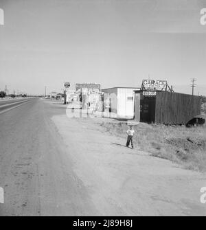 Tra Tulare e Fresno, California. Lungo l'autostrada US 99 a Highway City. [Segni che fanno pubblicità alla benzina; papà e amp; negozio di Ma's Beacon; birra, vino e generi alimentari; 7up; Dr Pepper; automobili usate; carica della batteria; saldatura; parti automatiche Foto Stock