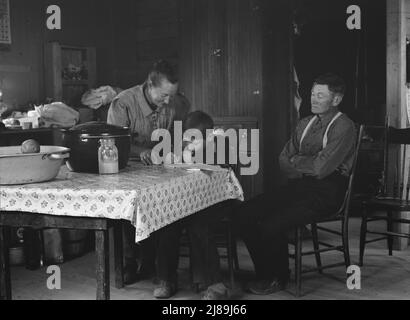 La famiglia Wardlow nella loro casa seminterrato dugout la domenica. Il ragazzo più giovane copia una ricetta per sua madre. Dead Ox Flat, contea di Malheur, Oregon. Foto Stock