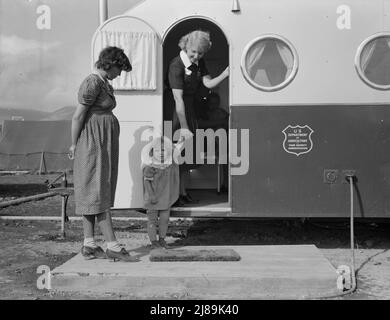 La giovane madre porta il suo bambino nella clinica del rimorchio il giorno in cui il medico sarà nel campo per esaminare alcuni dei bambini. Campo mobile FSA (Farm Security Administration). Merrill, contea di Klamath, Oregon. Foto Stock