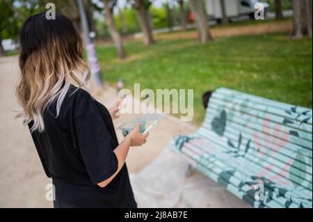 Il giovane illustratore locale Irene Terradas dipinge una panca di legno al popolare Jose Antonio Labordetta Park, durante l'iniziativa artistica urbana 'Bancos de Color Foto Stock